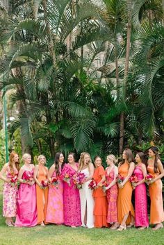 a group of women standing next to each other in front of palm trees and flowers