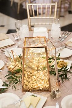 the table is set with plates and silverware, gold napkins, and glass containers