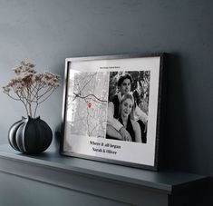 a black vase sitting on top of a mantle next to a framed photo and flowers