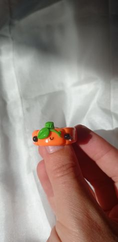 a hand holding an orange toy car with a green leaf on it's top