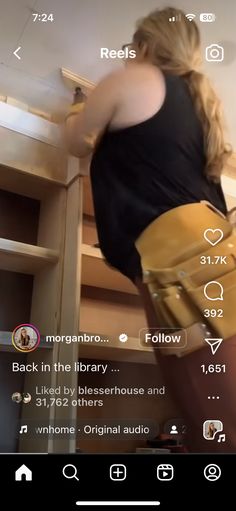 a woman is standing in front of a book shelf holding a yellow purse and looking at her phone