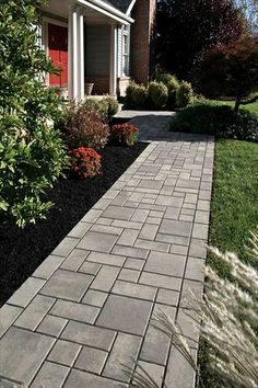 a brick walkway in the middle of a garden area with shrubs and flowers on either side