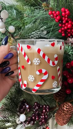 a woman holding a glass mug filled with hot chocolate and candy canes on top of a christmas tree