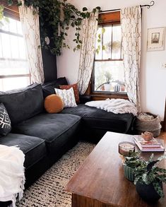 a living room with black couches and plants on the windowsill, coffee table