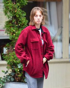 a woman is walking down the street with her hands in her pockets and wearing a red jacket