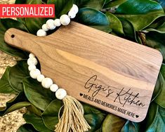 personalized wooden cutting board with tassels and name engraved on the side, surrounded by greenery