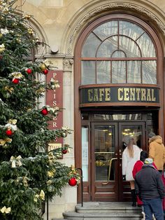 people are standing outside the entrance to a cafe in front of a christmas tree with red ornaments on it