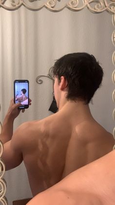 a shirtless man taking a selfie in front of a mirror with his cell phone