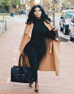 a woman is walking down the sidewalk carrying a black purse and coat over her shoulders