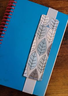 a notebook with a bookmark made out of fabric and leaves on the cover, sitting on a wooden table