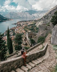 a woman is sitting on the steps leading up to an old castle with a lake and mountains in the background