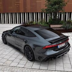 a grey sports car parked in front of a building with a bench on the side