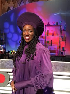 a woman in a purple gown and hat standing next to a white piano on stage