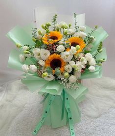 a bouquet of sunflowers and other flowers is wrapped in green ribbon on a white surface