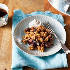 a white plate topped with fruit and granola next to a cup of coffee on top of a wooden table