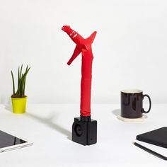 a red sculpture sitting on top of a white table next to a cup and cell phone