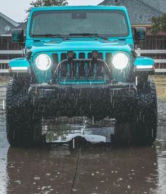 a blue jeep is driving in the rain with its headlights on and it's hood up