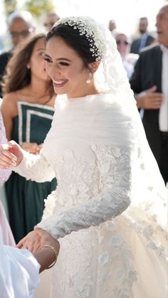 a woman in a wedding dress smiles as she holds the hand of another woman who is wearing a veil