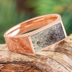 a rose gold ring with black and white stone inlays sits on top of a piece of wood