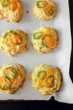 six biscuits with cheese and jalapenos sitting on top of a piece of parchment paper