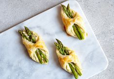 three asparagus wrapped in puff pastry on a white plate with a marble surface