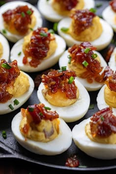 deviled eggs with bacon and ketchup are on a black plate, ready to be eaten