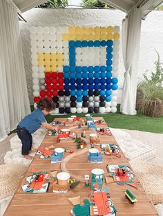 a young boy is playing with toys on a long table in front of a large balloon wall