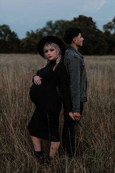 a pregnant woman standing next to a man in a field