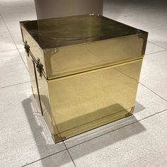 a shiny metal box sitting on top of a tile floor next to a trash can