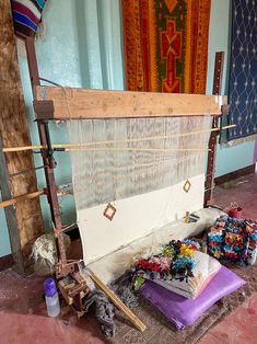 an old weaving machine is sitting on the floor in front of some rugs and other items