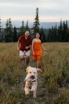 a man and woman are walking with their dog in the grass at sunset or sunrise