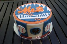 a new york mets cake sitting on top of a wooden table next to a bench