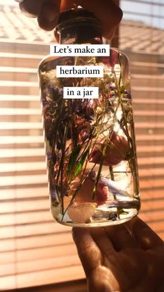 someone holding up a jar filled with plants and water in it's hand, saying let's make an herbarum in a jar