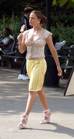 a woman in yellow is walking with an ice cream on her hand and looking at the camera