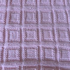 a pink crocheted blanket is laying on top of a tablecloth that has squares and lines drawn across it