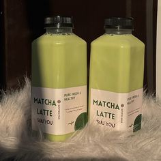 two bottles of matcha latte sitting on top of a white fur covered floor