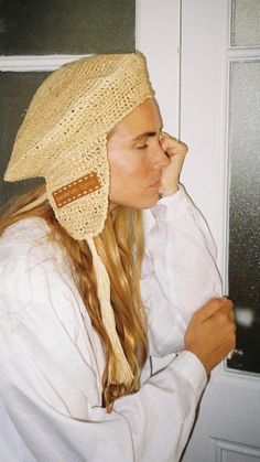 a woman with long hair wearing a hat and holding her hand up to her face