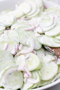 sliced cucumbers and onions in a white bowl with a wooden spoon on the side