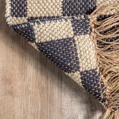 a blue and white checkered rug laying on top of a wooden floor with fringes