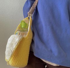 a person is holding a crocheted bag with a bottle in it and wearing brown pants