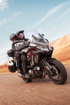 a man riding on the back of a motorcycle down a dirt road in the desert