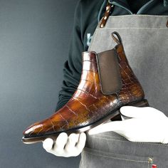 a man holding a pair of brown alligator - embossed leather shoes in his hands