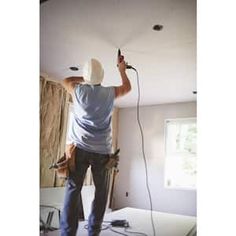 a man standing on top of a hard wood floor holding a power tool in his hand