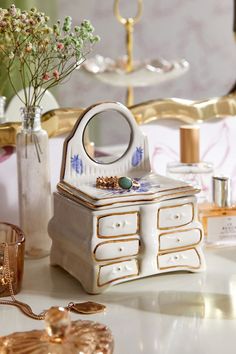 a white and gold jewelry box sitting on top of a table next to a vase filled with flowers