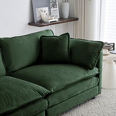 a green couch sitting in front of a window next to a white rug on top of a floor