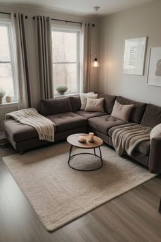 a living room with a sectional couch and coffee table in front of two large windows