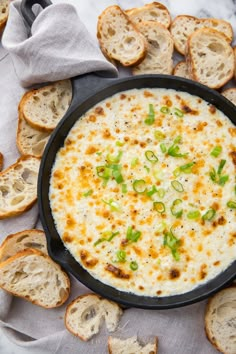 a black pan filled with cheese and green onions on top of bread slices in front of it