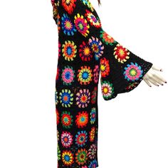 a woman wearing a black crochet dress with colorful flowers on it's sleeves