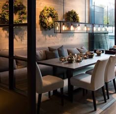 a dining room table and chairs with candles on them in front of a wall decorated with wreaths