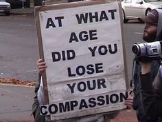 a man holding up a sign that says at what age did you lose your companion?